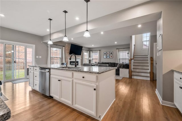 kitchen with stainless steel dishwasher, a sink, light wood-type flooring, white cabinets, and light stone countertops