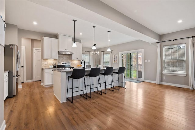 kitchen with stainless steel appliances, a breakfast bar area, under cabinet range hood, light wood-style floors, and recessed lighting