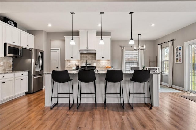 kitchen with stainless steel appliances, light wood-style flooring, backsplash, a kitchen island with sink, and a kitchen bar