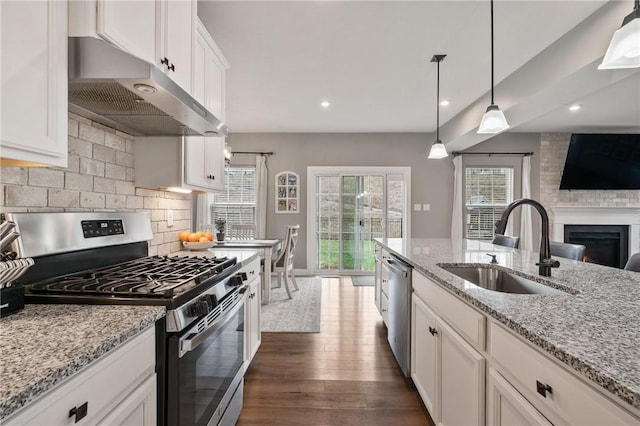 kitchen with stainless steel appliances, under cabinet range hood, a sink, white cabinets, and plenty of natural light