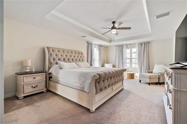 bedroom with a tray ceiling, light carpet, a ceiling fan, and baseboards