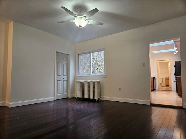 empty room featuring radiator heating unit, a ceiling fan, dark wood-type flooring, and baseboards