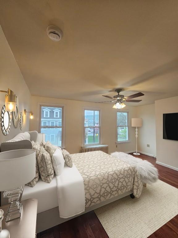 bedroom featuring radiator, dark wood-style floors, baseboards, and ceiling fan