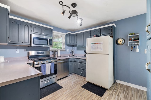 kitchen with appliances with stainless steel finishes, light wood-style floors, gray cabinets, a sink, and light countertops