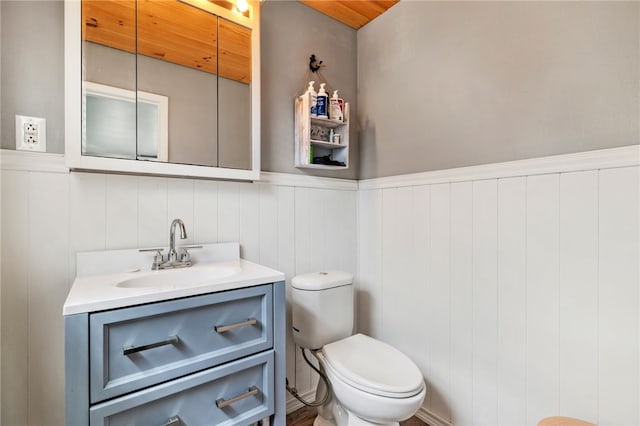 half bath featuring vanity, a wainscoted wall, toilet, and wood ceiling