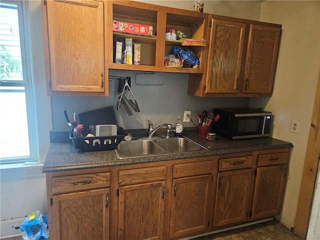 kitchen with black microwave, a sink, dark countertops, and open shelves