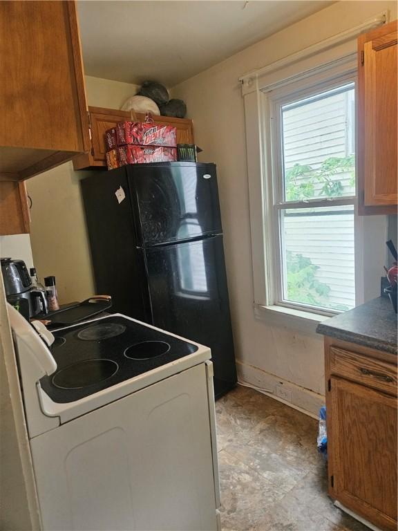 kitchen featuring electric range, brown cabinetry, dark countertops, and baseboards