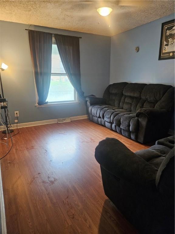 living room featuring a textured ceiling, wood finished floors, and baseboards