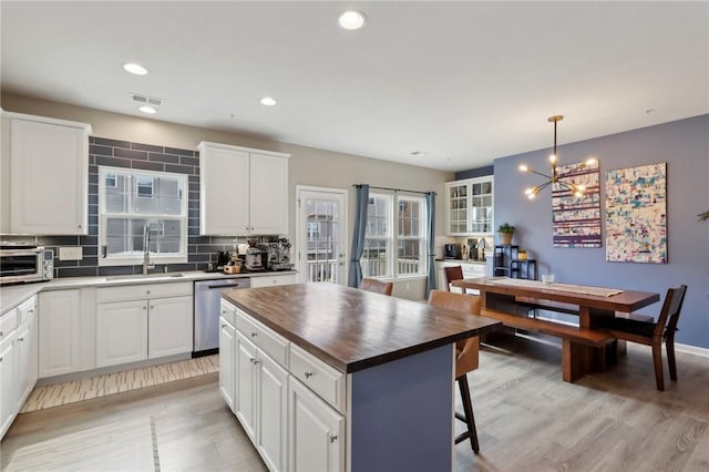 kitchen featuring stainless steel dishwasher, a sink, wooden counters, light wood-style flooring, and a chandelier