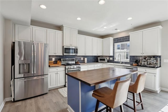 kitchen with appliances with stainless steel finishes, wooden counters, backsplash, a kitchen breakfast bar, and recessed lighting