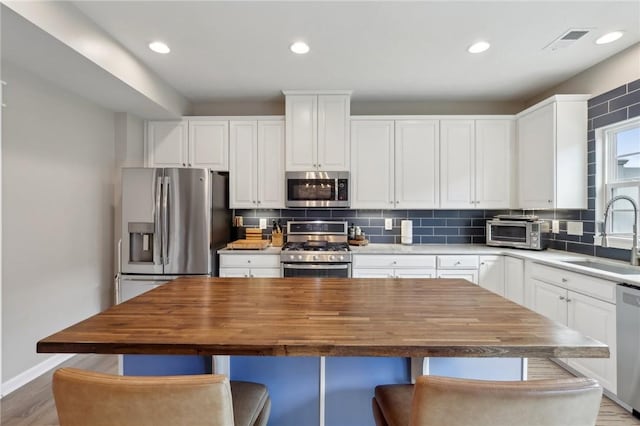 kitchen with stainless steel appliances, a sink, butcher block counters, backsplash, and recessed lighting