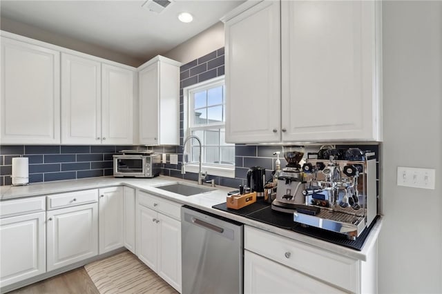kitchen with stainless steel dishwasher, a sink, backsplash, and white cabinetry