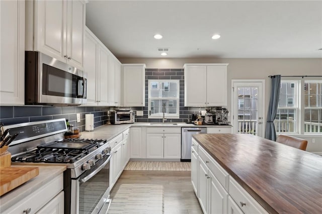 kitchen featuring appliances with stainless steel finishes, wooden counters, a sink, tasteful backsplash, and white cabinets