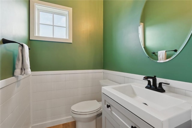 bathroom featuring a wainscoted wall, toilet, vanity, and tile walls