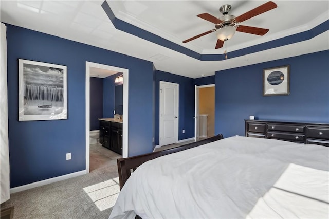 carpeted bedroom with a raised ceiling, crown molding, baseboards, ensuite bath, and a ceiling fan