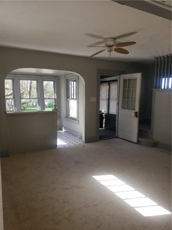 spare room featuring arched walkways, a ceiling fan, carpet flooring, and baseboards