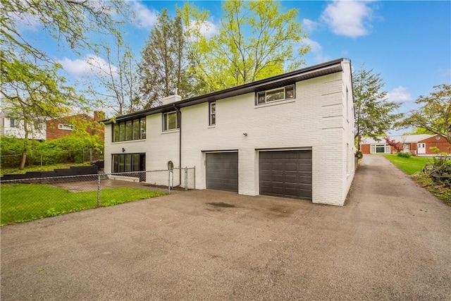 view of side of property featuring an attached garage, fence, and asphalt driveway