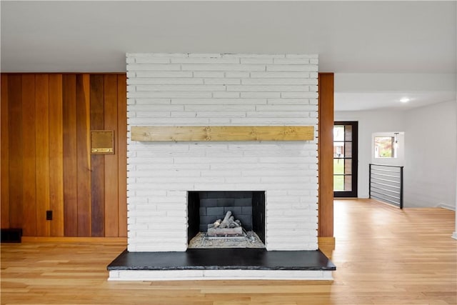 detailed view of wood finished floors, a brick fireplace, wooden walls, and baseboards