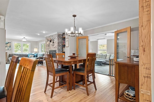 dining space featuring a brick fireplace, light wood-style floors, a chandelier, and ornamental molding