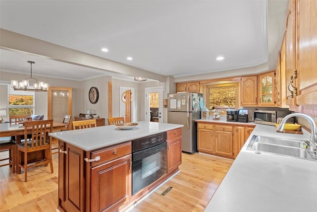 kitchen with a sink, stainless steel appliances, light wood-style flooring, a center island, and ornamental molding