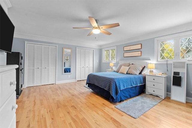bedroom with two closets, light wood finished floors, baseboards, a ceiling fan, and ornamental molding