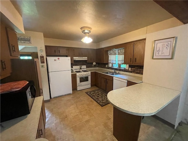 kitchen featuring white appliances, a sink, under cabinet range hood, a peninsula, and light countertops