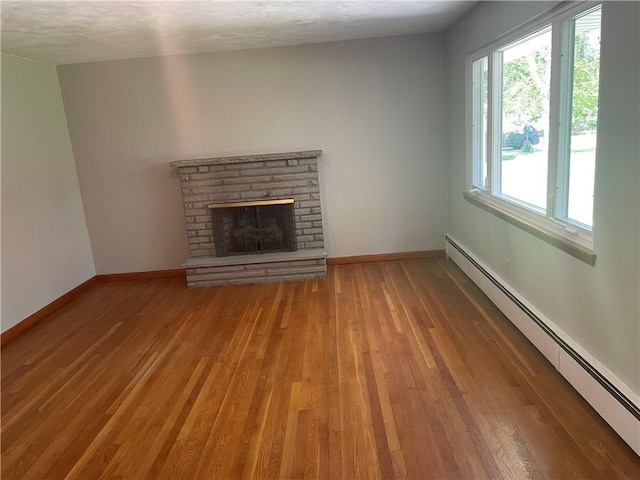 855 W Sanner St, Somerset Boro, PA 15501 - unfurnished living room featuring a baseboard heating unit, wood-type flooring, baseboards, a fireplace with raised hearth, and a textured ceiling