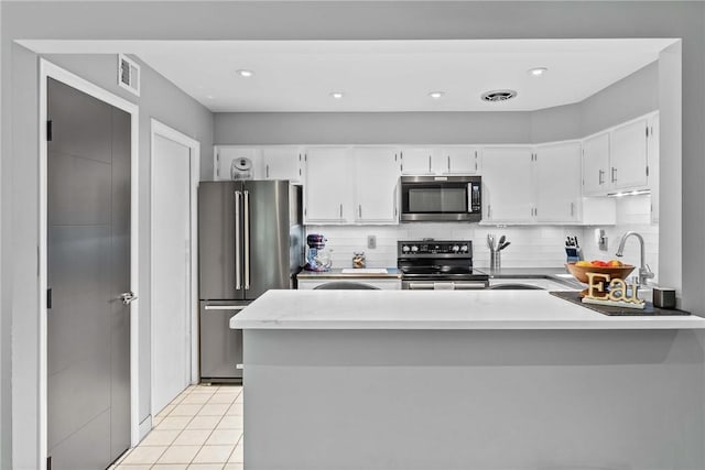 kitchen with stainless steel appliances, white cabinets, light countertops, a peninsula, and decorative backsplash