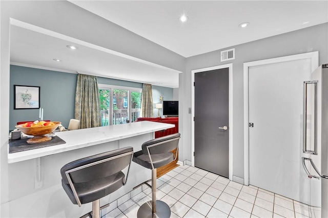kitchen featuring high end refrigerator, recessed lighting, a kitchen breakfast bar, light countertops, and light tile patterned floors