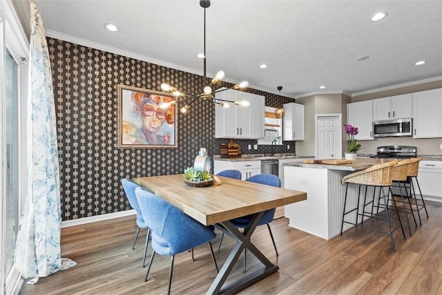 kitchen with appliances with stainless steel finishes, wallpapered walls, a kitchen island, ornamental molding, and white cabinetry