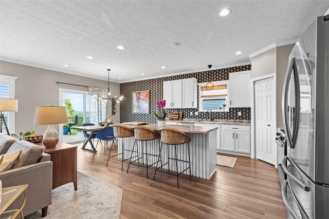 kitchen with freestanding refrigerator, crown molding, open floor plan, a textured ceiling, and a kitchen bar