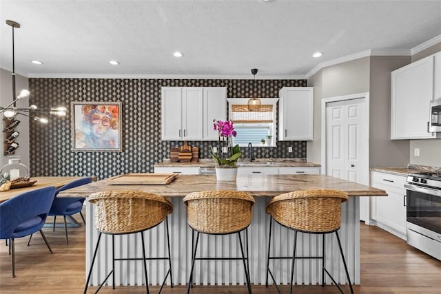 kitchen featuring appliances with stainless steel finishes, crown molding, white cabinets, wood finished floors, and a kitchen island