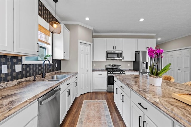 kitchen with appliances with stainless steel finishes, a sink, white cabinets, pendant lighting, and light stone counters