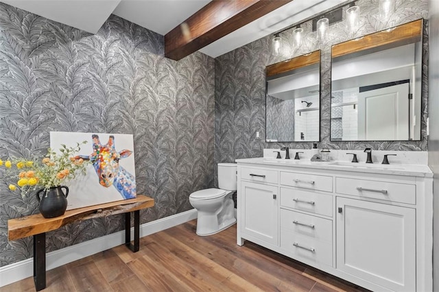 bathroom with wallpapered walls, wood finished floors, toilet, double vanity, and baseboards