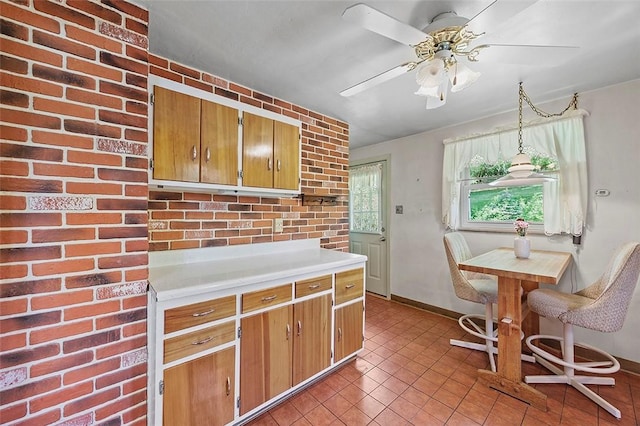 kitchen with light countertops, light tile patterned floors, ceiling fan, brown cabinets, and baseboards