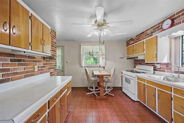 kitchen with white range with gas stovetop, a sink, light countertops, under cabinet range hood, and a ceiling fan