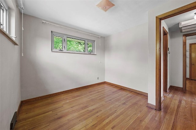 spare room featuring light wood-style floors, baseboards, and an AC wall unit