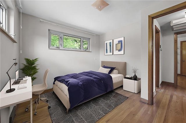 bedroom with wood finished floors, baseboards, and an AC wall unit