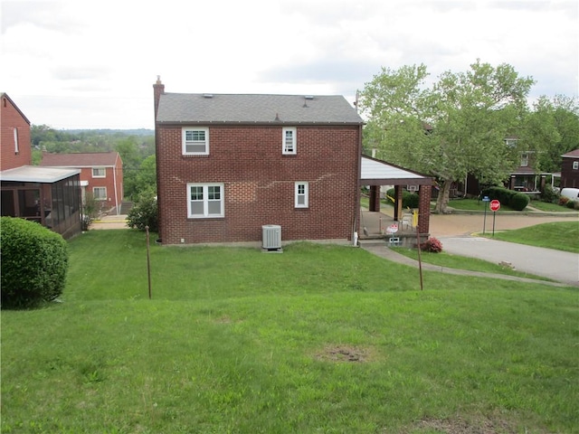 rear view of property featuring central AC unit, a yard, a chimney, and brick siding
