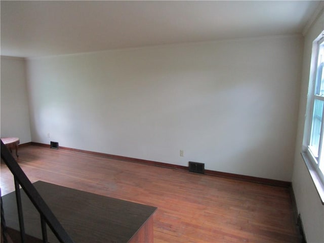 unfurnished room featuring light wood-style floors, ornamental molding, healthy amount of natural light, and baseboards