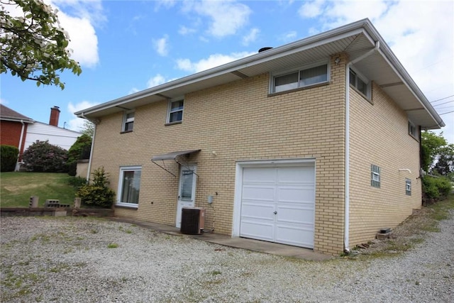 rear view of property with a garage, central air condition unit, brick siding, and driveway