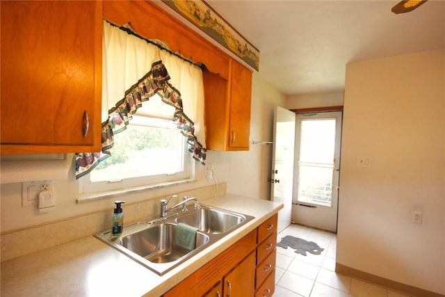 kitchen with a sink, brown cabinets, light countertops, and light tile patterned flooring