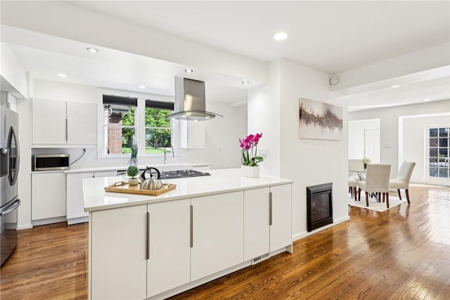 kitchen with island range hood, stainless steel appliances, white cabinetry, wood finished floors, and recessed lighting