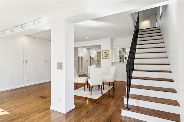 stairway with wood finished floors, track lighting, and baseboards