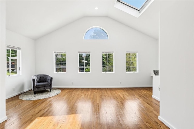 unfurnished room featuring a skylight, light wood finished floors, healthy amount of natural light, and high vaulted ceiling