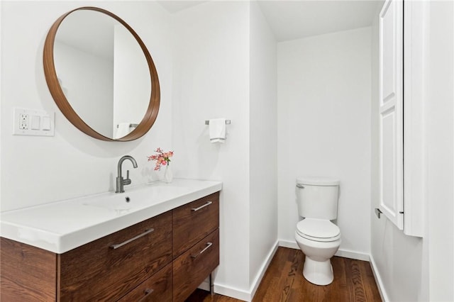 half bathroom with wood finished floors, toilet, vanity, and baseboards