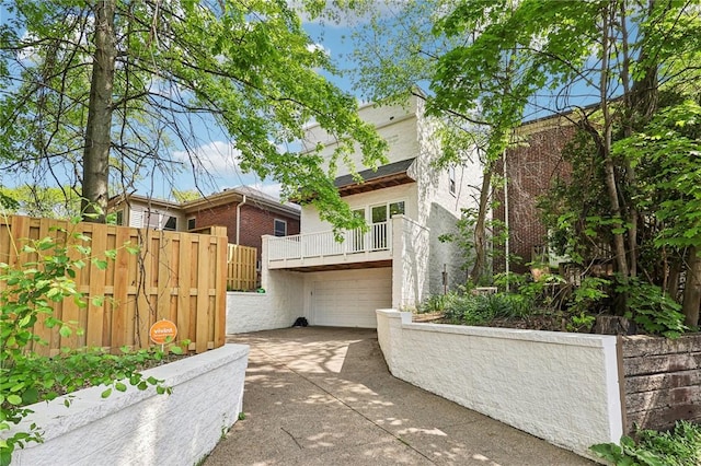 view of patio featuring a garage, driveway, fence, and a balcony