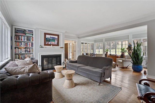 living room with crown molding, a glass covered fireplace, wood finished floors, and built in shelves