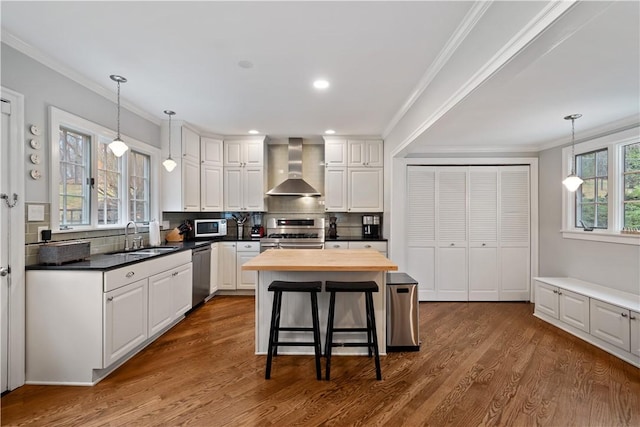 kitchen featuring wall chimney range hood, appliances with stainless steel finishes, a sink, butcher block counters, and white cabinetry