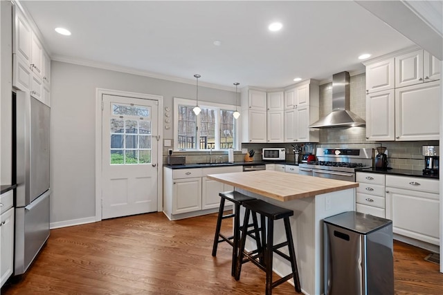 kitchen with wall chimney exhaust hood, butcher block countertops, appliances with stainless steel finishes, ornamental molding, and decorative backsplash